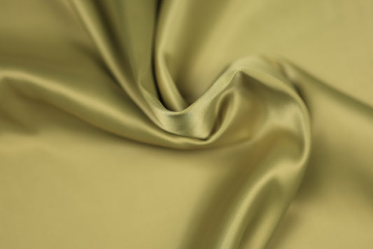 Satinstoff in edlem Helloliv mit weicher Drapierung und seidig glänzender Oberfläche – ideal für Sommerkleider, Accessoires und stilvolle Dekorationen
