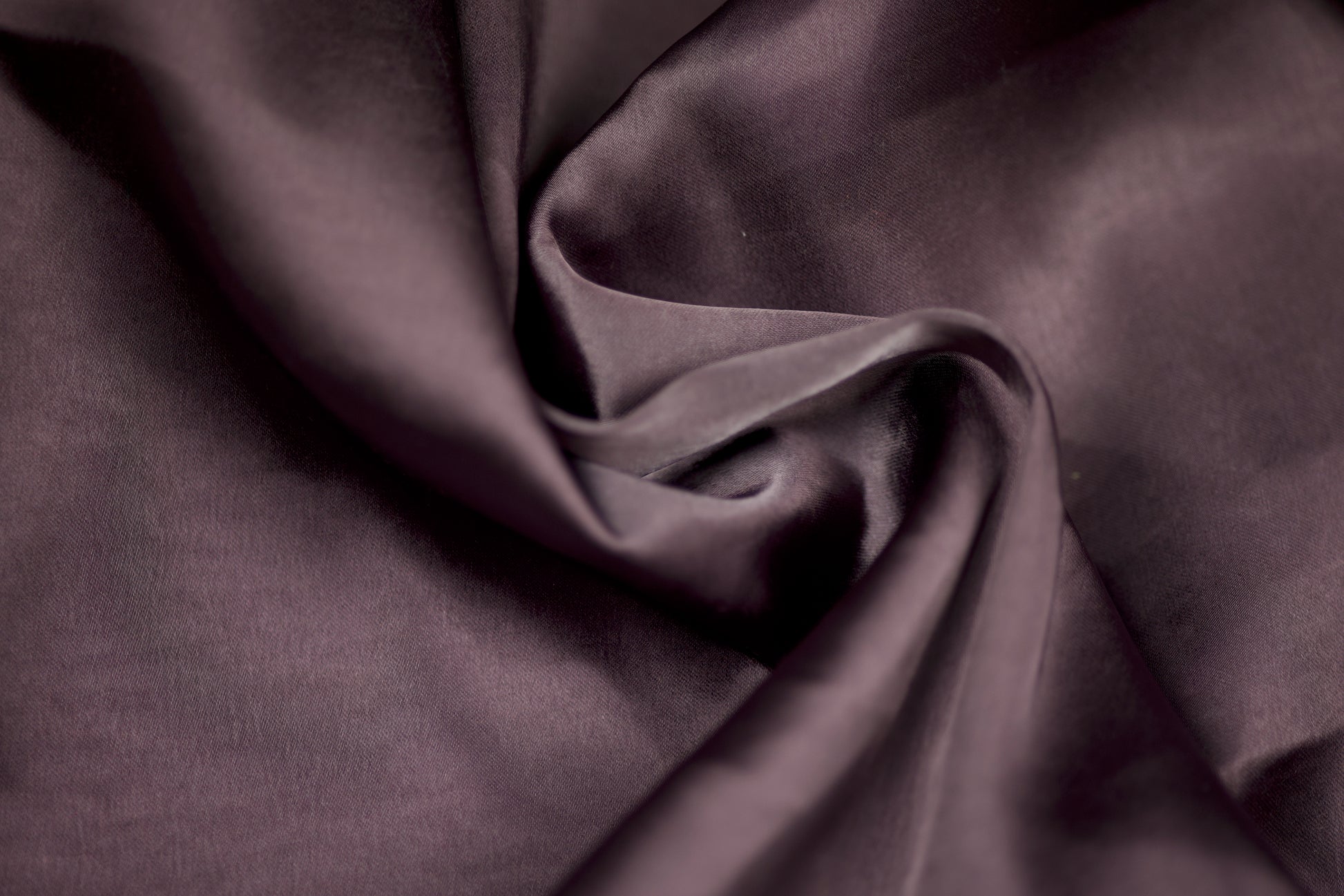 Nahaufnahme eines luxuriösen Satinstoffs in pflaumenfarbener Optik mit seidigem Glanz und weichem Faltenwurf – ideal für elegante Kleidung und kreative Projekte.