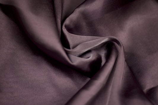 Nahaufnahme eines luxuriösen Satinstoffs in pflaumenfarbener Optik mit seidigem Glanz und weichem Faltenwurf – ideal für elegante Kleidung und kreative Projekte.