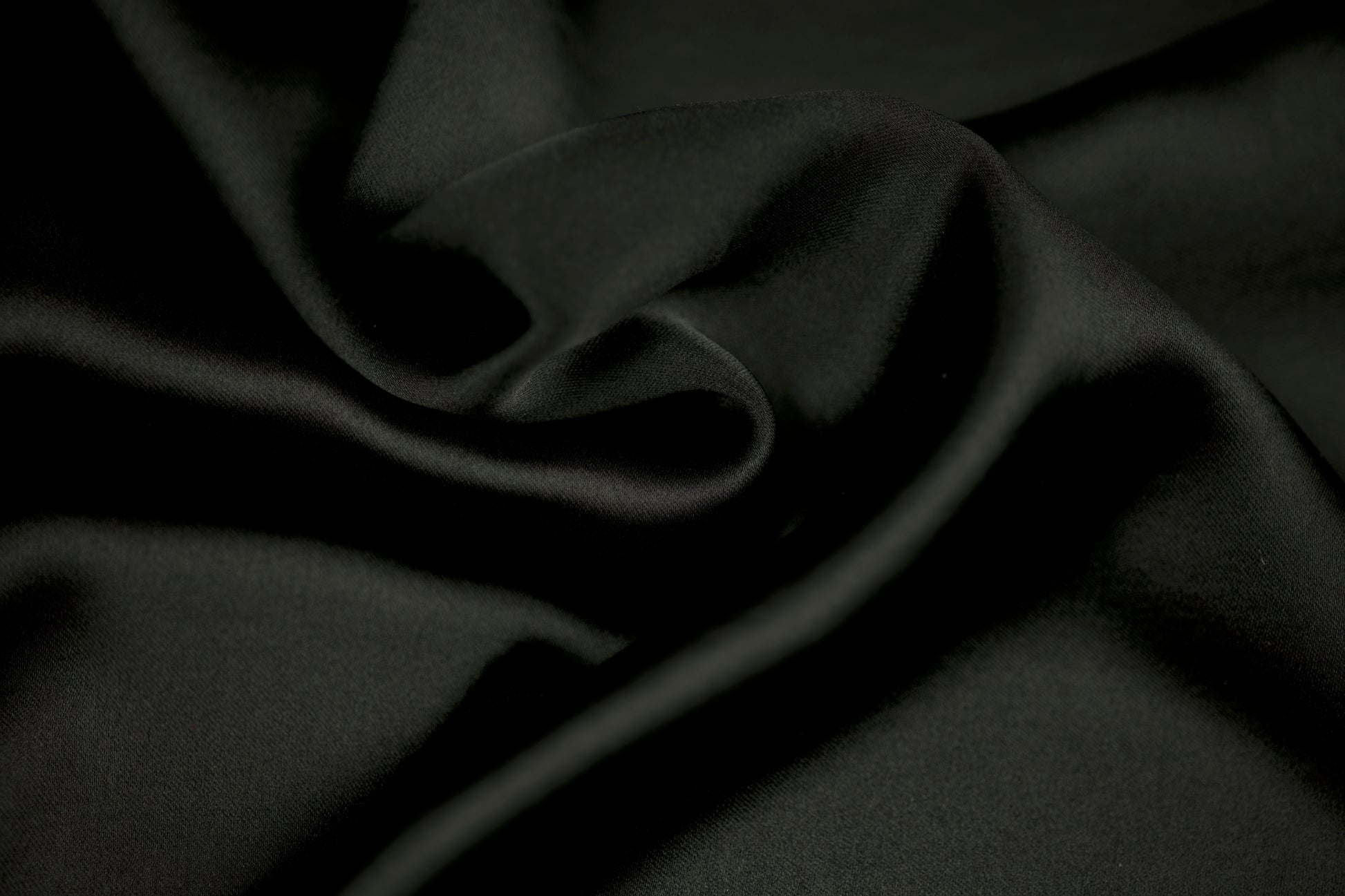 Nahaufnahme eines luxuriösen Satinstoffs in elegantem Schwarz mit weichem Faltenwurf und seidig glänzender Oberfläche.