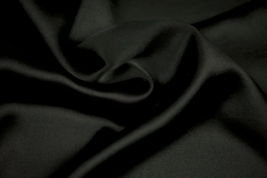 Nahaufnahme eines luxuriösen Satinstoffs in elegantem Schwarz mit weichem Faltenwurf und seidig glänzender Oberfläche.